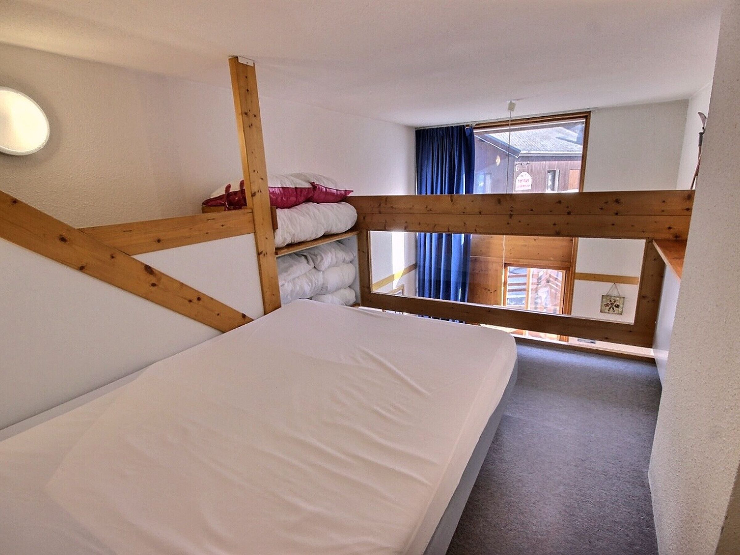 Une chambre de dortoir avec des lits superposés, une fenêtre avec des rideaux et une vue sur l’extérieur.