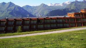 Une rangée de chalets en bois dotés de grandes fenêtres, se dressant sur un fond de montagnes et de ciel dégagé.