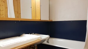 Une salle de bain avec un lavabo blanc, une baignoire et des panneaux de bois aux murs.