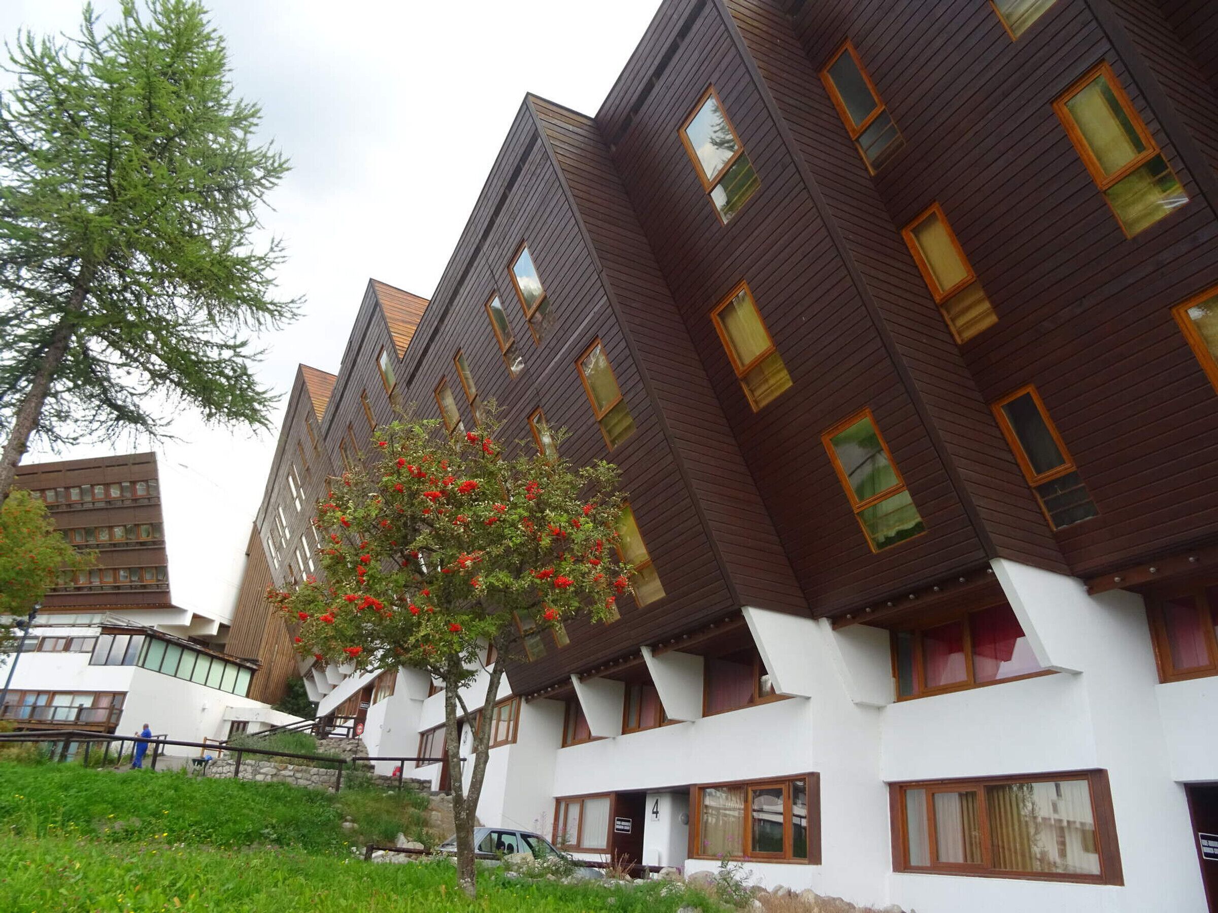 Un edificio moderno con diverse finestre e un albero con fiori rossi di fronte.