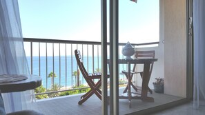 Un balcone con vista sul mare, una chitarra, un tavolo con un vaso e una sedia.