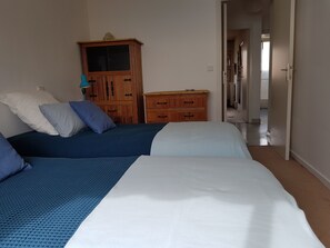 Une chambre avec deux lits, des meubles en bois et un couloir menant à une autre pièce.
