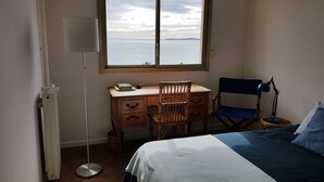 A bedroom with a bed, a desk with a chair, a lamp, and a view of the sea through a window. - Balcony facing the sea, 3 rooms (76m2), private park DEPARTURE ON SATURDAY EXCLUSIVELY (Cagnes-Sur-Mer)
