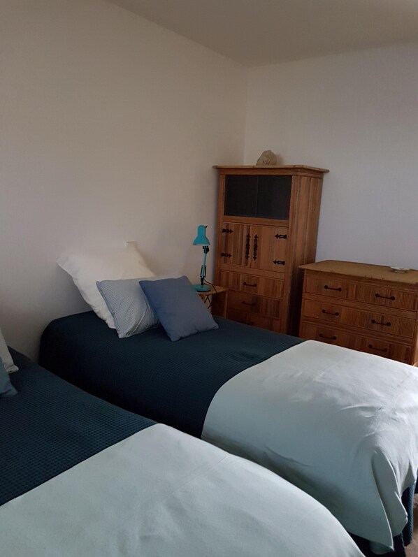Un dormitorio con dos camas, un armario de madera y una mesita de noche con lámpara.