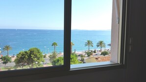 A view from a window overlooking a beach with palm trees and a clear blue sea. - Balcony facing the sea, 3 rooms (76m2), private park DEPARTURE ON SATURDAY EXCLUSIVELY (Cagnes-Sur-Mer)