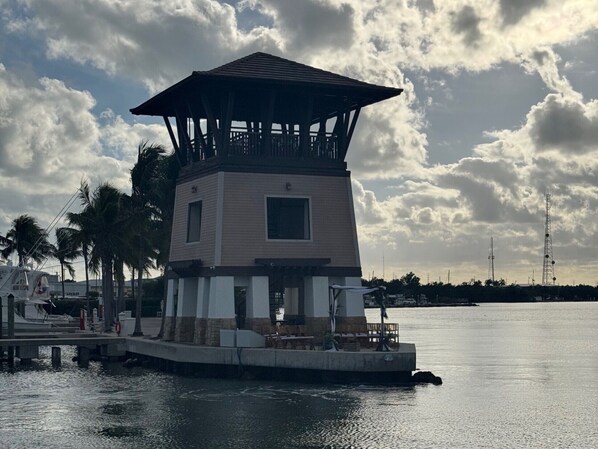 A waterfront structure with a central tower, surrounded by palm trees and a calm body of water.