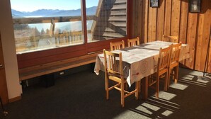 Un coin repas avec une table dressée pour six personnes, des chaises en bois et une vue sur les montagnes à travers de grandes fenêtres.