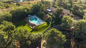 An aerial view of a property with a swimming pool, lush greenery, and a house with a tiled roof.