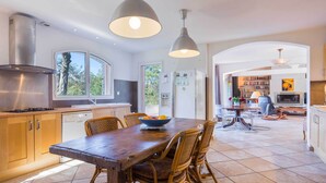A modern kitchen with a wooden dining table, wicker chairs, and pendant lighting.