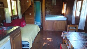 Una camera compatta in stile baita, con un letto, angolo cottura, zona pranzo e bagno.