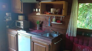 Cucina compatta con mobili in legno, forno a microonde, lavandino e finestra con vista sul verde.