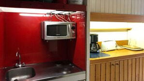 Une cuisine compacte dotée d’un évier en acier inoxydable, d’un four à micro-ondes et d’une machine à café, le tout installé sur un plan de travail en bois.
