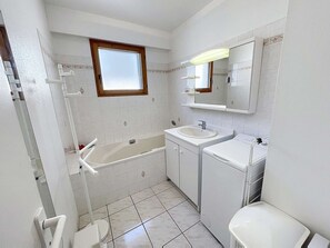 Et badeværelse med badekar, vask, toilet og et vindue.