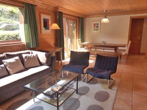 Una sala de estar acogedora con un sofá, dos sillones, una mesa de centro de vidrio, una mesa de comedor y un banco.