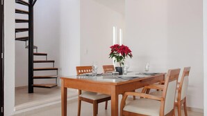 Un comedor con una mesa de madera dispuesta para cuatro personas, sillas, una planta en maceta y una escalera.