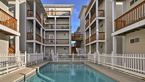 A multi-story residential building with a central swimming pool, white railings, and balconies with wooden railings.