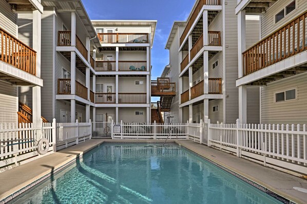 A multi-story residential building with a central swimming pool, white railings, and balconies with wooden railings.