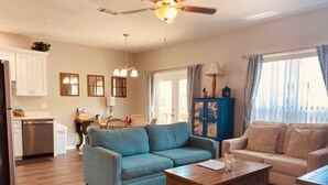 A living room with a blue sofa, beige sofa, wooden coffee table, and a dining area with wicker chairs.