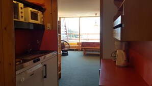 Cocina compacta con armarios de madera, microondas, cafetera y vistas a un balcón con banco.