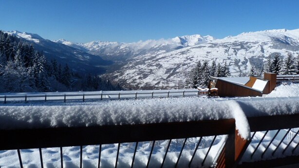 Paisaje montañoso cubierto de nieve, con una estructura de madera y una cerca de metal en primer plano.