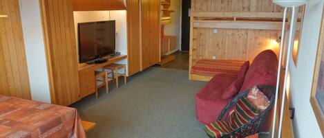 A compact room with a television, a small table, a sofa, and a bunk bed.