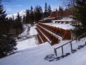 A snow-covered ski lift with a wooden structure and metal supports, surrounded by snow-covered trees and a mountain in the background.