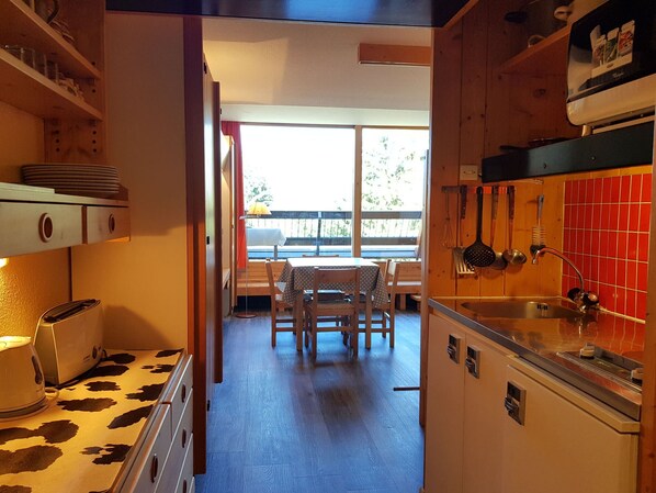 A compact kitchen with a dining area, wooden cabinets, and a view through the window.