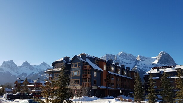 A multi-story hotel with a snow-covered roof, large windows, and a balcony. - Amazing views ! Beautiful 2 bed/2 bath condo.,Free WiFi/Cable. Prime location! (Canmore)