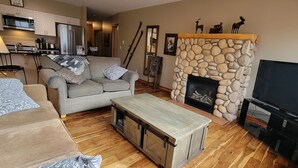 A cozy living room with a stone fireplace, a television, and a sofa with patterned cushions. - Amazing views ! Beautiful 2 bed/2 bath condo.,Free WiFi/Cable. Prime location! (Canmore)