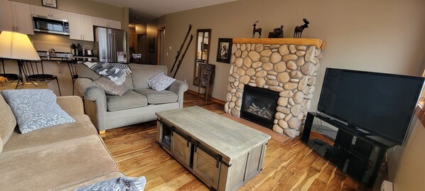 A cozy living room with a stone fireplace, a television, and a sofa with patterned cushions.