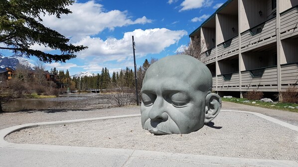 Une grande sculpture en pierre, située dans un espace aménagé, avec un bâtiment en arrière-plan.