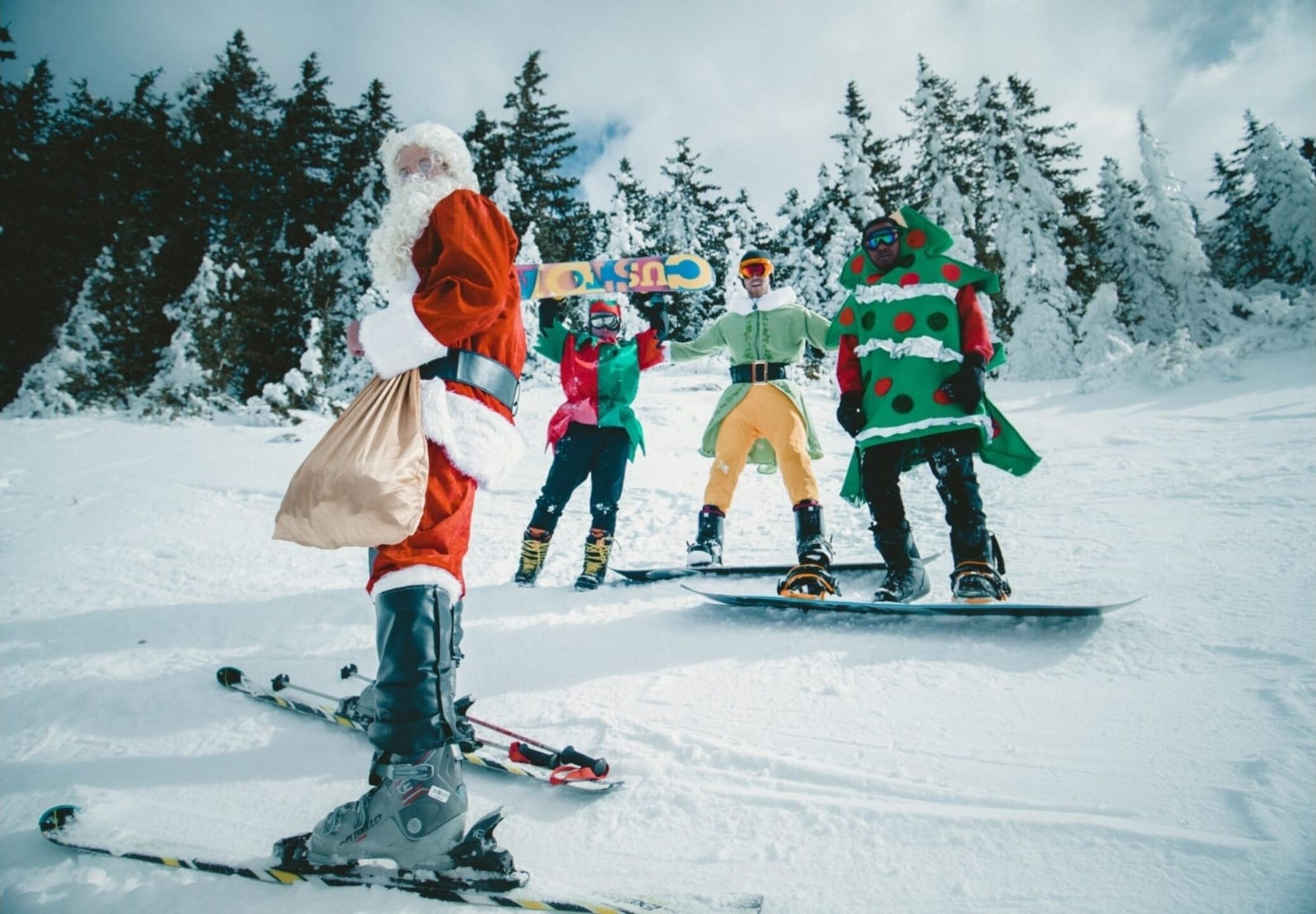 Un grupo de personas esquiando y practicando snowboard en un paisaje nevado con árboles al fondo.