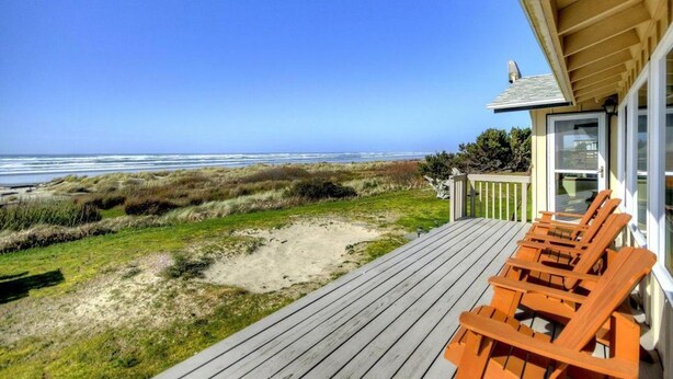 Eine Holzterrasse mit Liegestühlen mit Blick auf einen Strand mit Dünen und dem Meer.