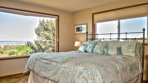 Ein Schlafzimmer mit einem großen Bett, einem Fenster mit Meerblick und einem gerahmten Bild an der Wand.