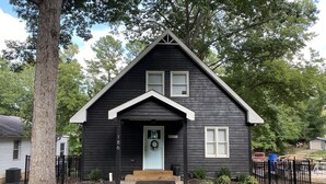 A black wooden house with a white door and two windows, surrounded by trees and a gravel driveway. - Cozy 2 Bed 2 Bath waterfront cottage on beautiful High Rock Lake- fully updated (Lexington)
