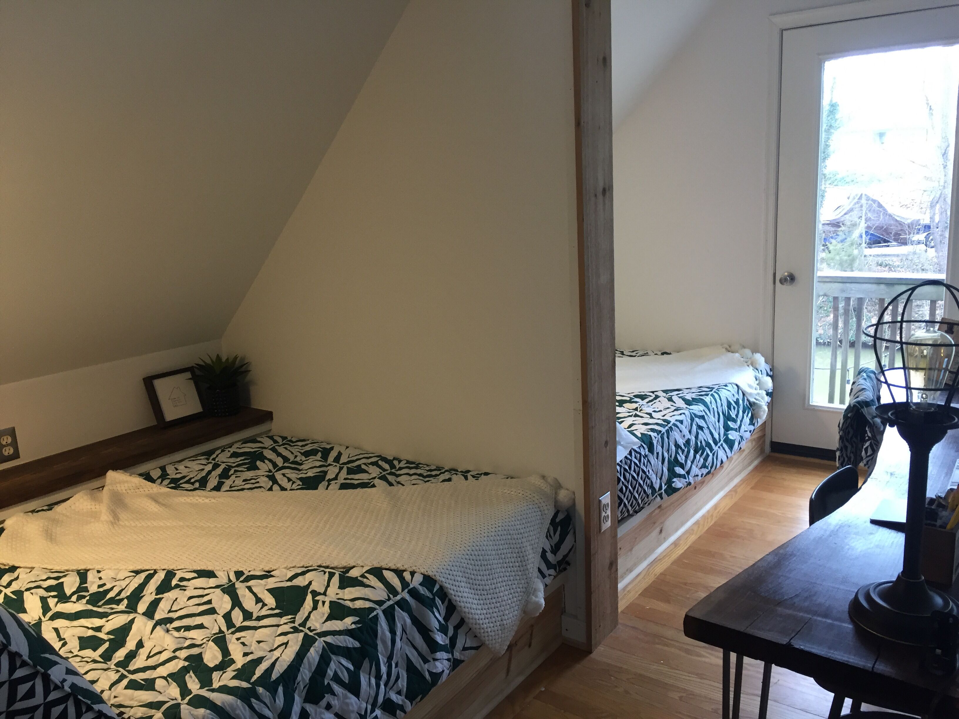 Une petite pièce agréable et chaleureuse, avec deux lits, un plancher en bois, une fenêtre donnant sur un beau paysage et une petite table avec une lampe.