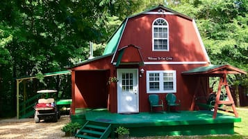 Cozy cabin with a porch, featuring a swing set and golf cart parking.