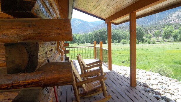 A wooden deck with a view of a green field and mountains. - Post Office Ranch  Log Cabin - rates subject to change for groups over 2 people (Salida)