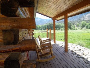 A wooden deck with a view of a green field and mountains. - Post Office Ranch Log Cabin - rates subject to change for groups over 2 people (Salida)