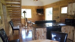 A rustic cabin interior with a wooden dining table, chairs, a fireplace, a kitchen with a stove and microwave, and a wooden staircase. - Post Office Ranch  Log Cabin - rates subject to change for groups over 2 people (Salida)