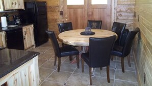 A wooden cabin interior with a dining table surrounded by chairs, a kitchen area with cabinets and appliances, and a double door entrance. - Post Office Ranch  Log Cabin - rates subject to change for groups over 2 people (Salida)