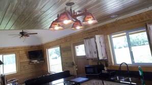 A rustic cabin interior with a wooden ceiling, a ceiling fan, a dining area with a table and chairs, a kitchen with a microwave, and a large window. - Post Office Ranch  Log Cabin - rates subject to change for groups over 2 people (Salida)