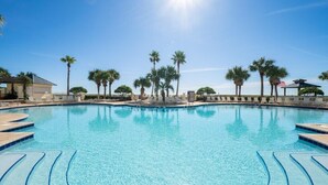A clear blue swimming pool with steps leading into it, surrounded by palm trees and lounge chairs.