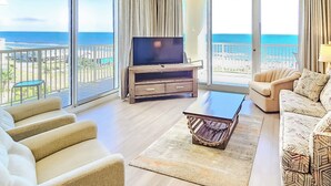A living room with a TV, sofa, armchair, and a view of the ocean.