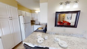 Une cuisine avec des meubles blancs, un plan de travail en granit et un miroir qui reflète un canapé rouge.