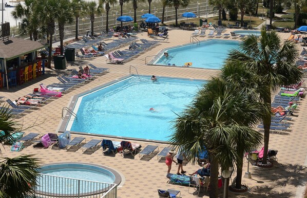 A pool area with multiple swimming pools, sun loungers, and palm trees.