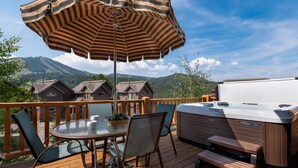 A deck with a hot tub, a table with chairs, and an umbrella.