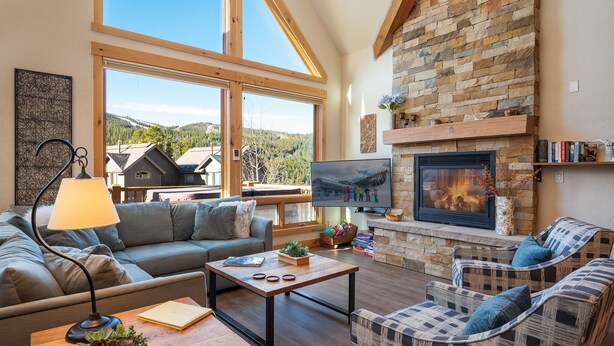 A cozy living room with a stone fireplace, large windows, and comfortable seating.