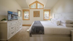 A bedroom with a bed, a TV on a dresser, and three windows.
