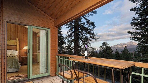 A wooden deck with a glass door leading to a bedroom, a wooden table with chairs, and a mountain view. - Walk to Ski & Village, Views Condo, Pool & Spa 315 (Mammoth Lakes)
